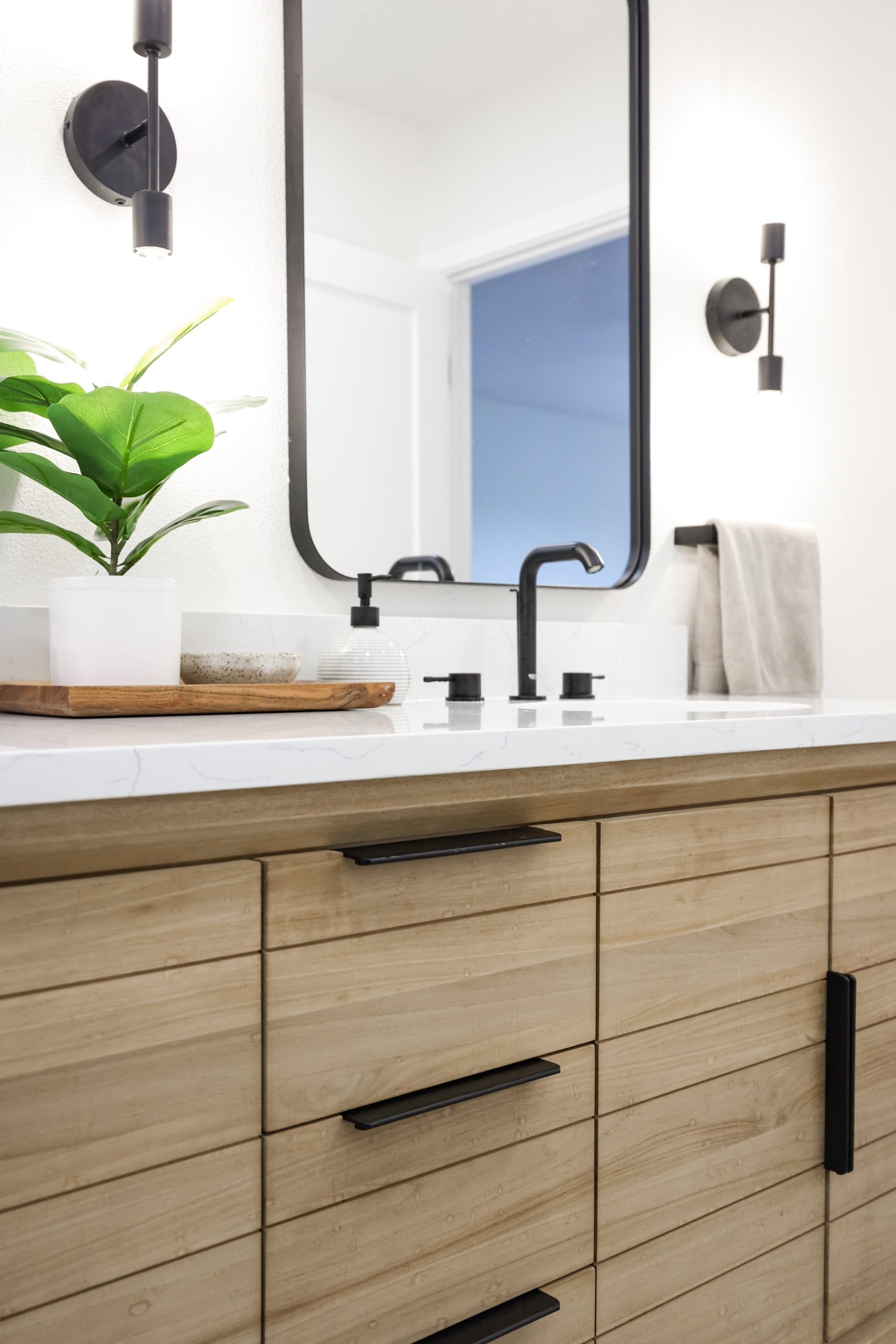 Bathroom vanity with slatted oak cabinets, quartz top and black faucet