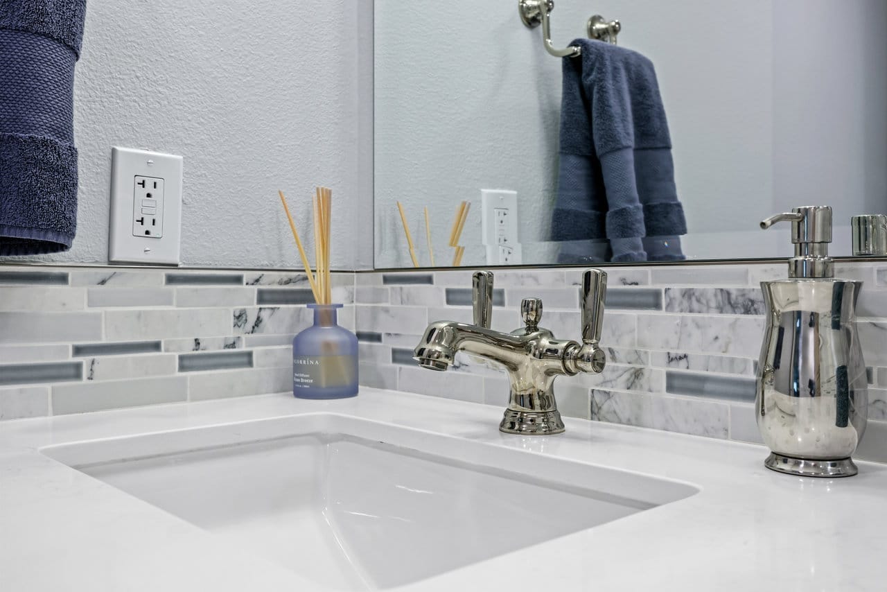 bathroom vanity with white quartz undermount sink, chrome faucet and marble-look tile mosaic backsplash