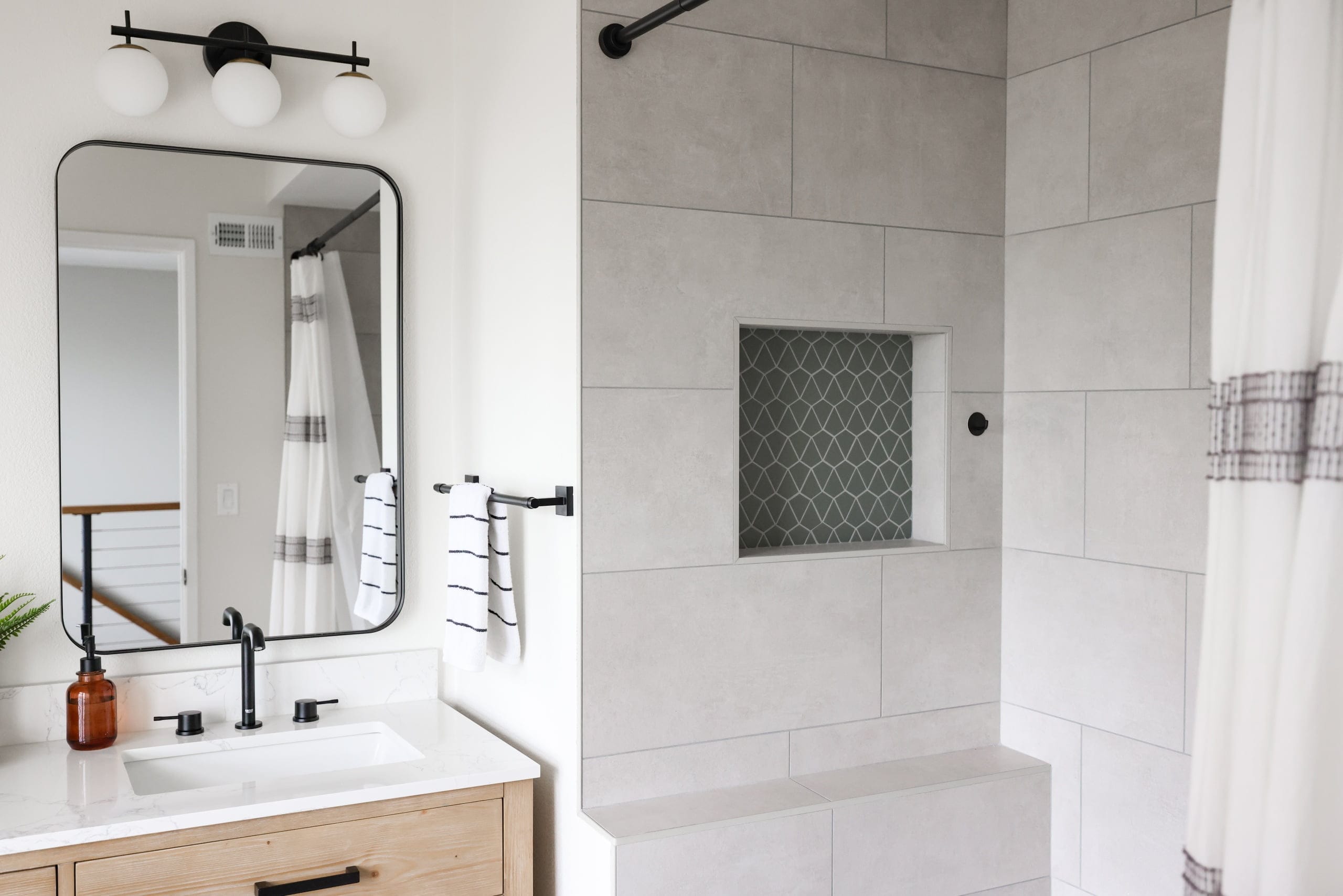 Bathroom with black-framed mirror, oak vanity, and gray tiled tub surround