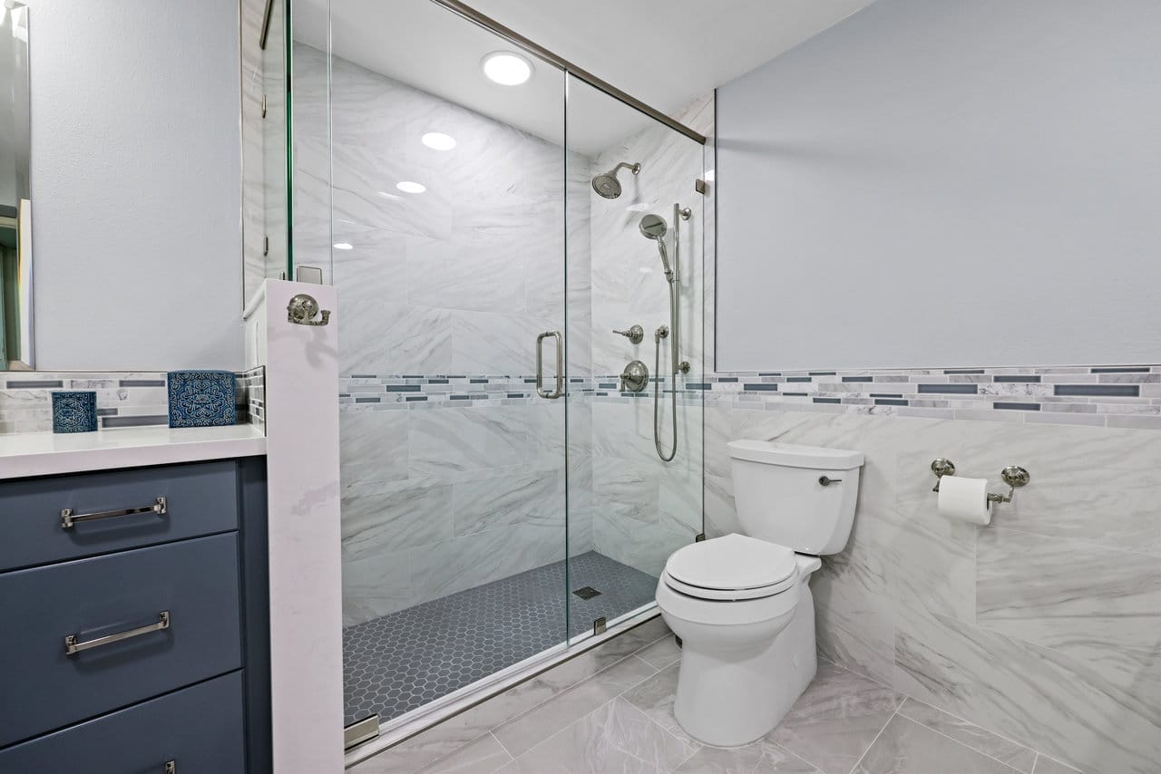 bathroom with frameless glass walk-in shower, navy vanity and marble-look porcelain tile