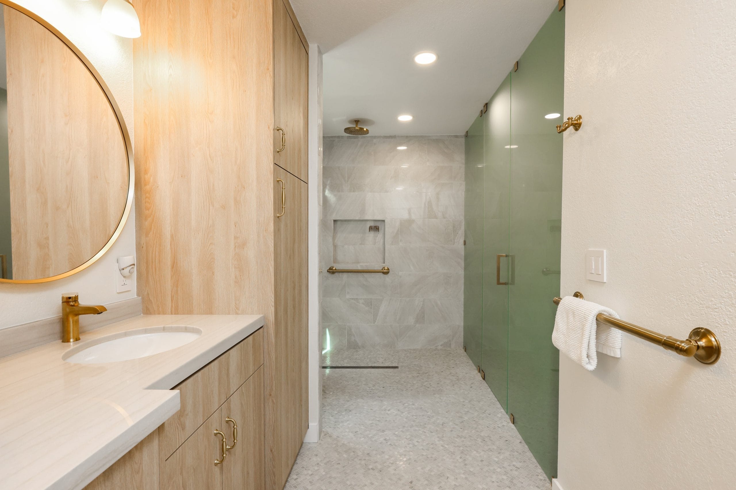 Bathroom with oak vanity, glass-enclosed marble shower and sage accent wall