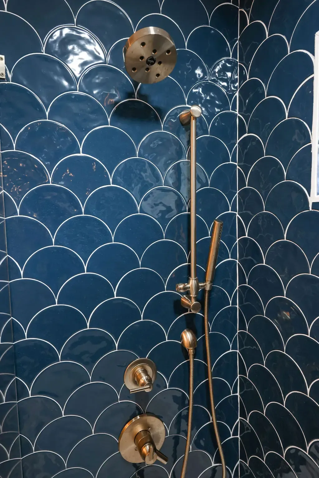Blue scalloped tile shower wall featuring brushed brass rainfall head and slide bar