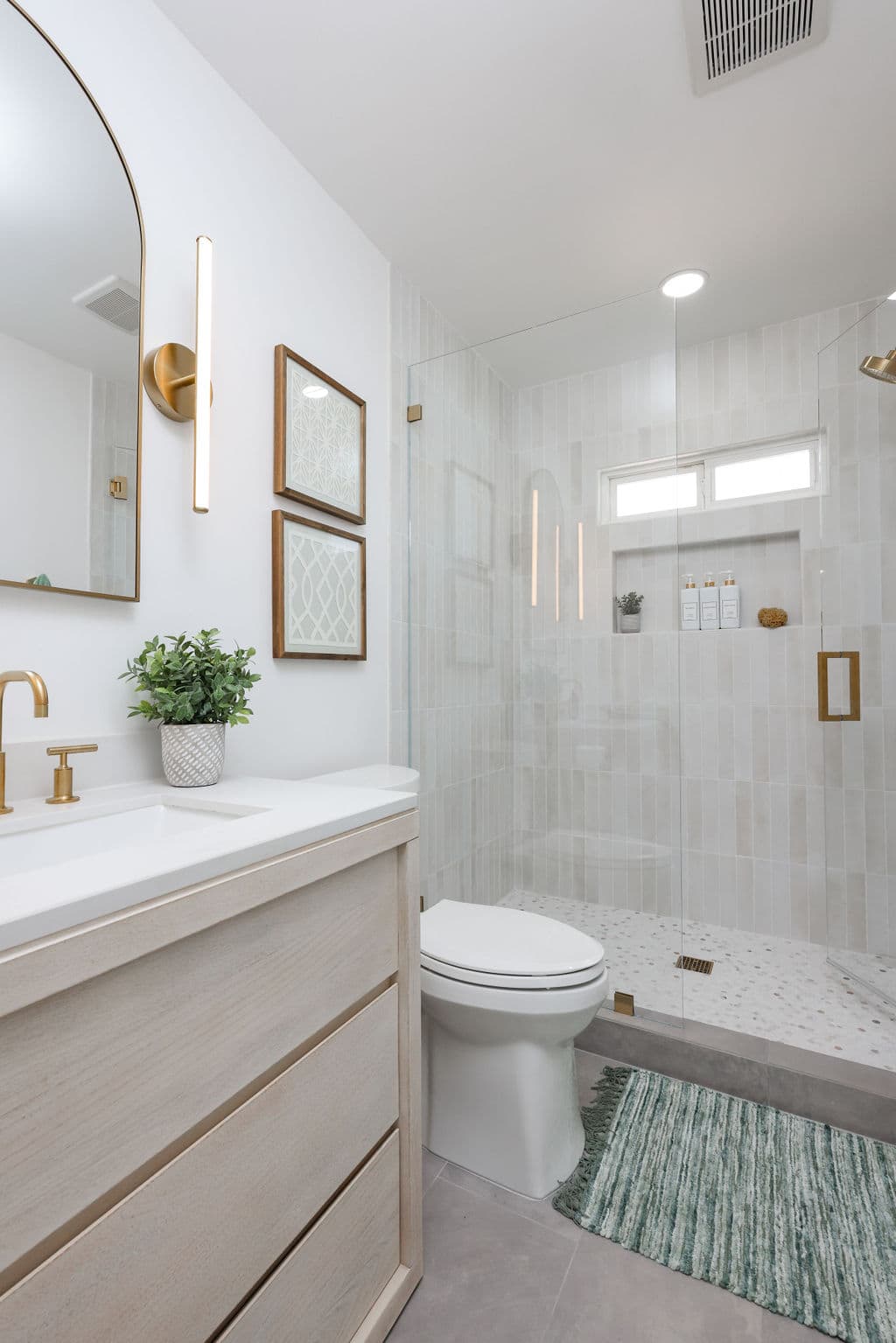 bright bathroom featuring frameless glass shower, oak floating vanity and gold accents