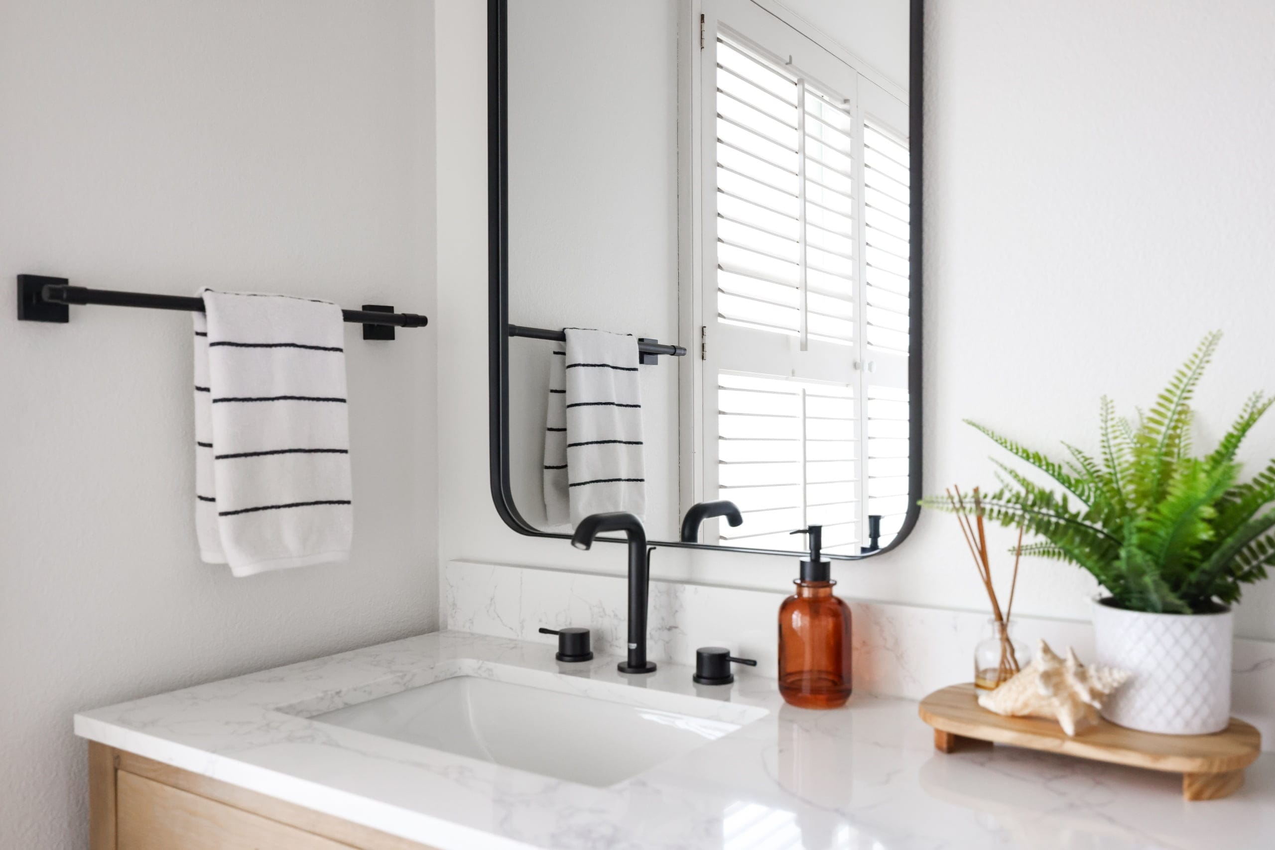 Bright bathroom vanity with marble counter, black faucet, and framed mirror