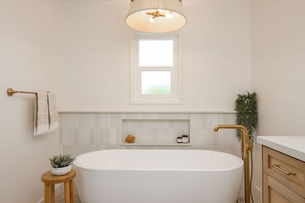 Bright bathroom with freestanding tub, brass floor faucet, and zellige tile wainscot