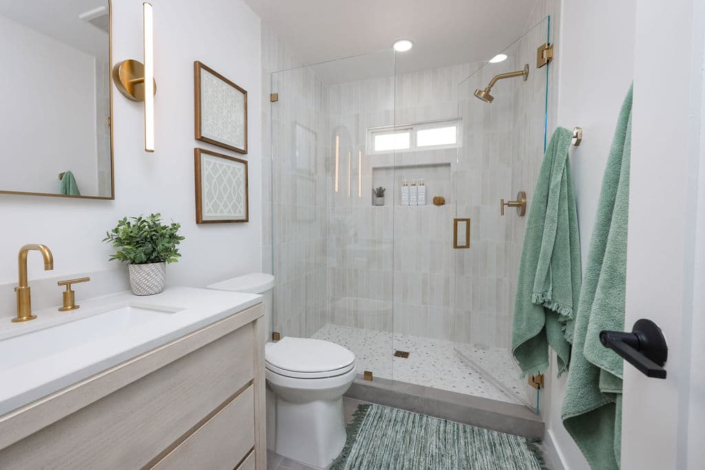 bright bathroom with white oak floating vanity, brushed gold fixtures and walk-in shower