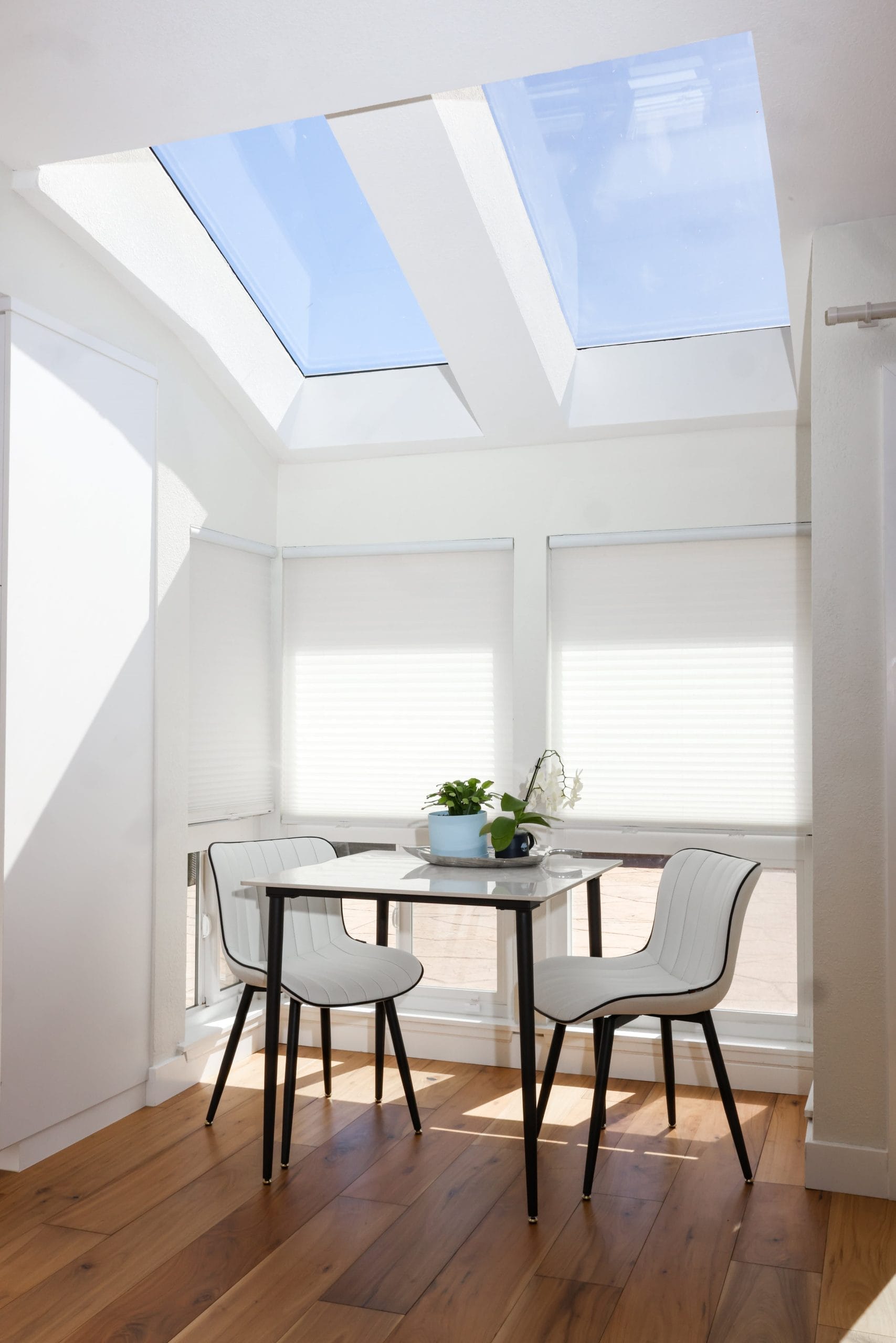 Bright breakfast corner under angled skylights with white table and chairs