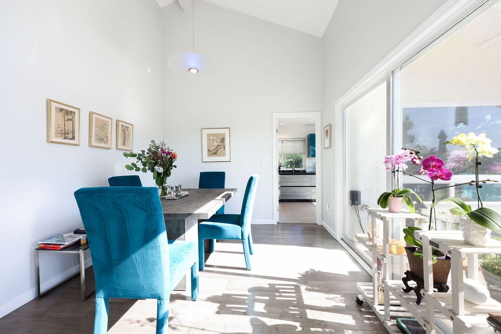 Bright dining nook with teal velvet chairs, gray wood table, and sliding glass doors
