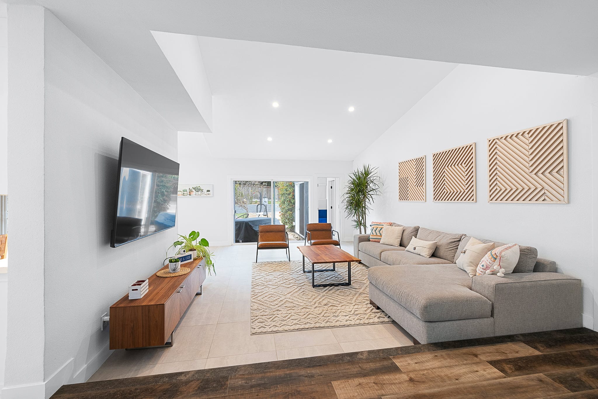 Bright open living room with gray sectional, wood slat art and vaulted ceiling