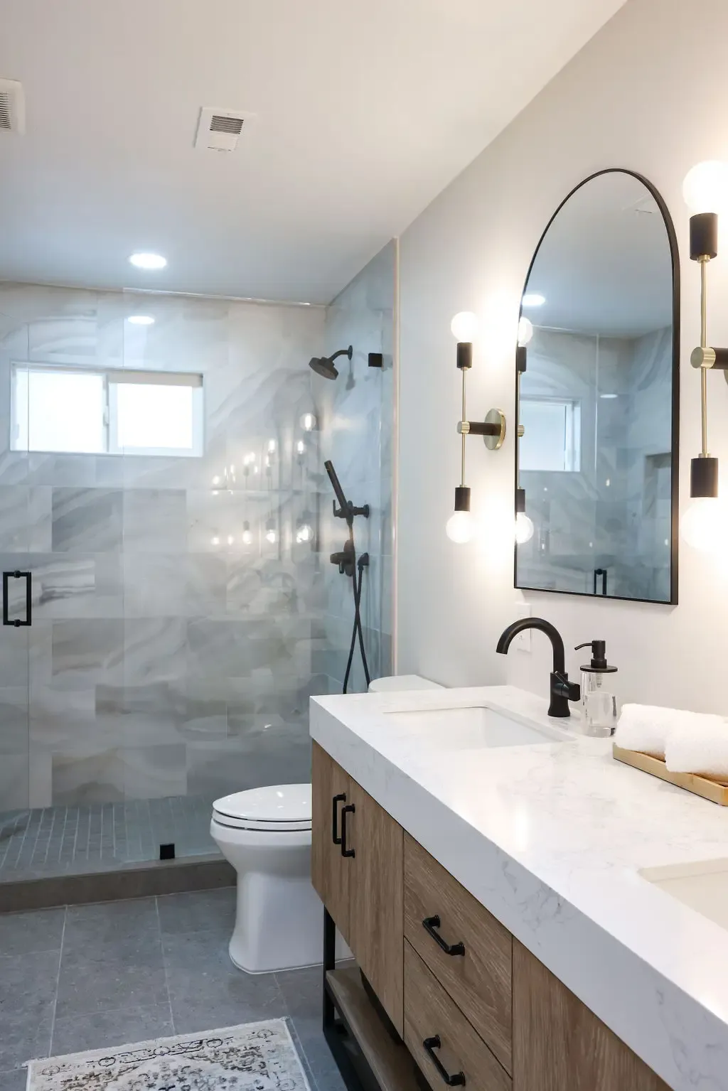 Bright remodeled bathroom with wood vanity, quartz counter and marble-tile shower