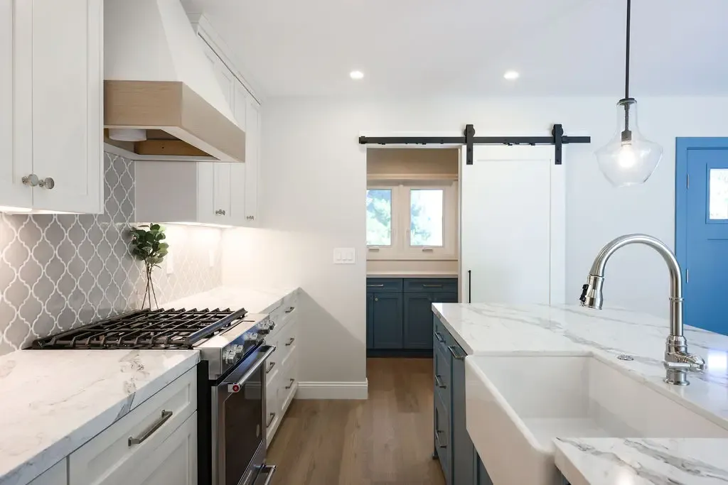 Bright remodeled kitchen featuring marble farmhouse sink, gas range, and sliding barn door