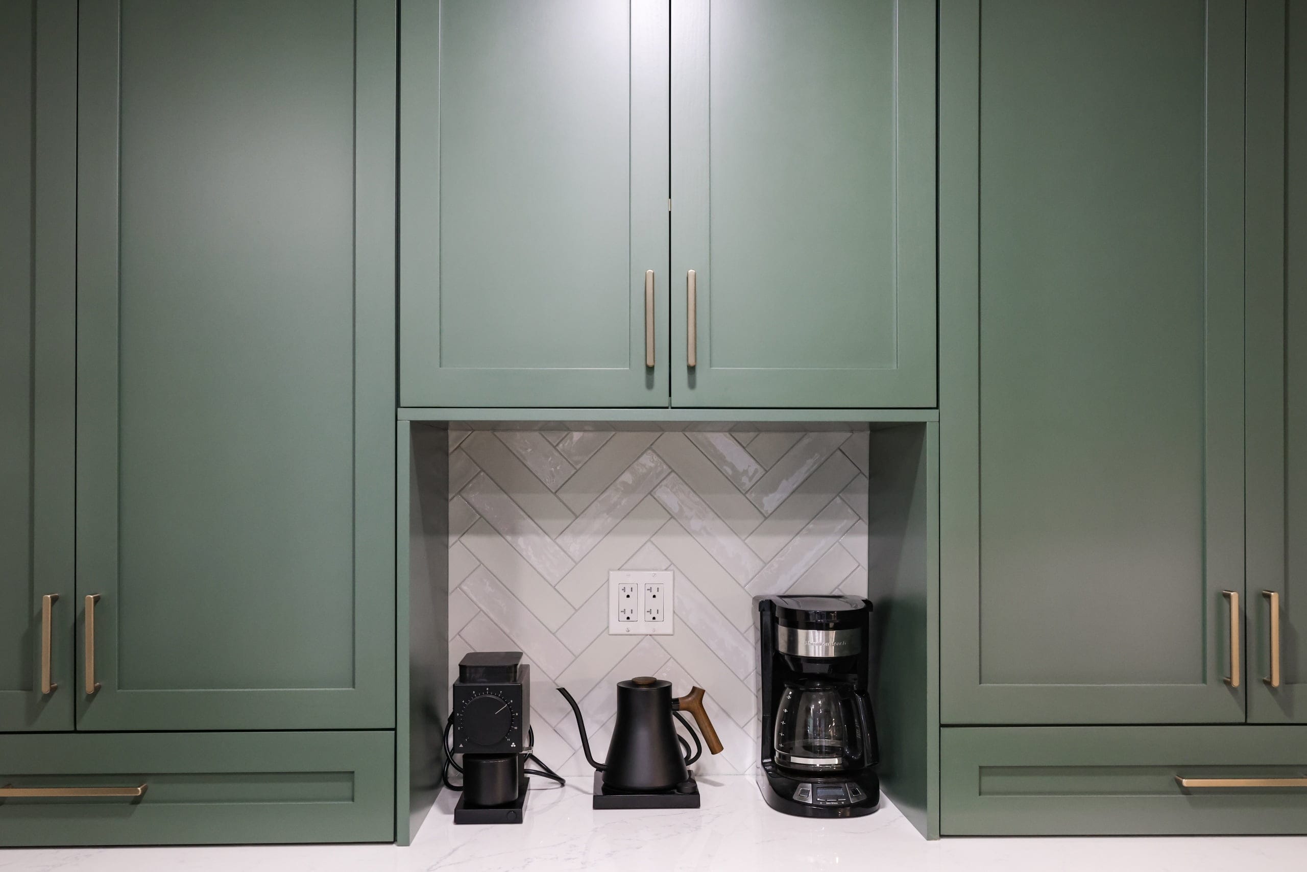 Built-in coffee station nook with marble herringbone tile set between deep green cabinets