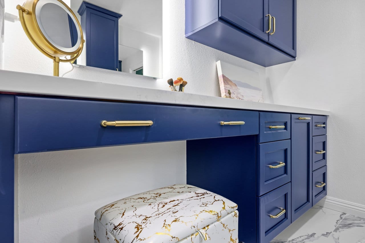 built-in navy makeup desk with quartz top, gold pulls and veined marble upholstered stool