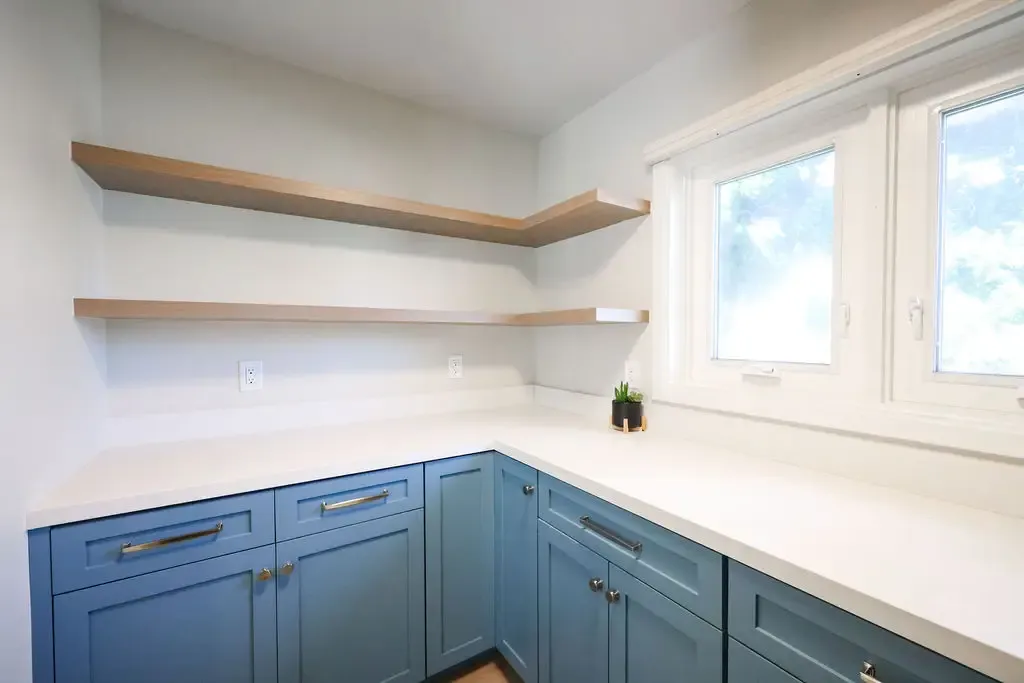 Butler's pantry with blue cabinets, white countertops, and floating wood wall shelves