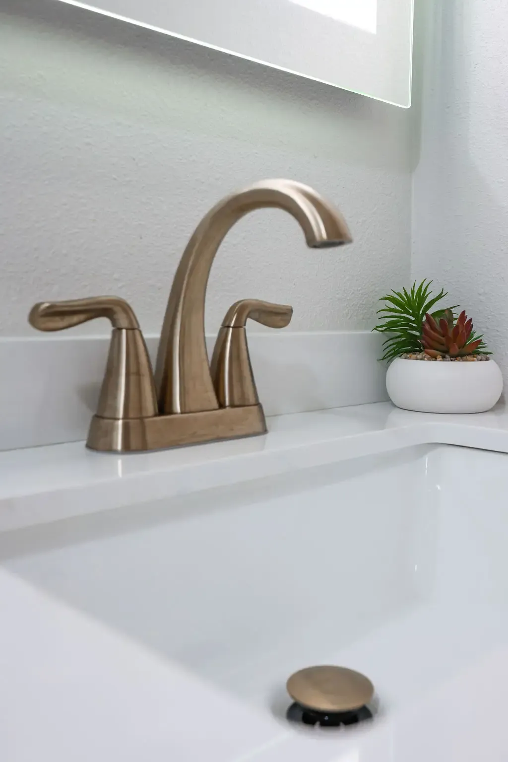 Close-up of brushed bronze widespread faucet on white quartz vanity countertop