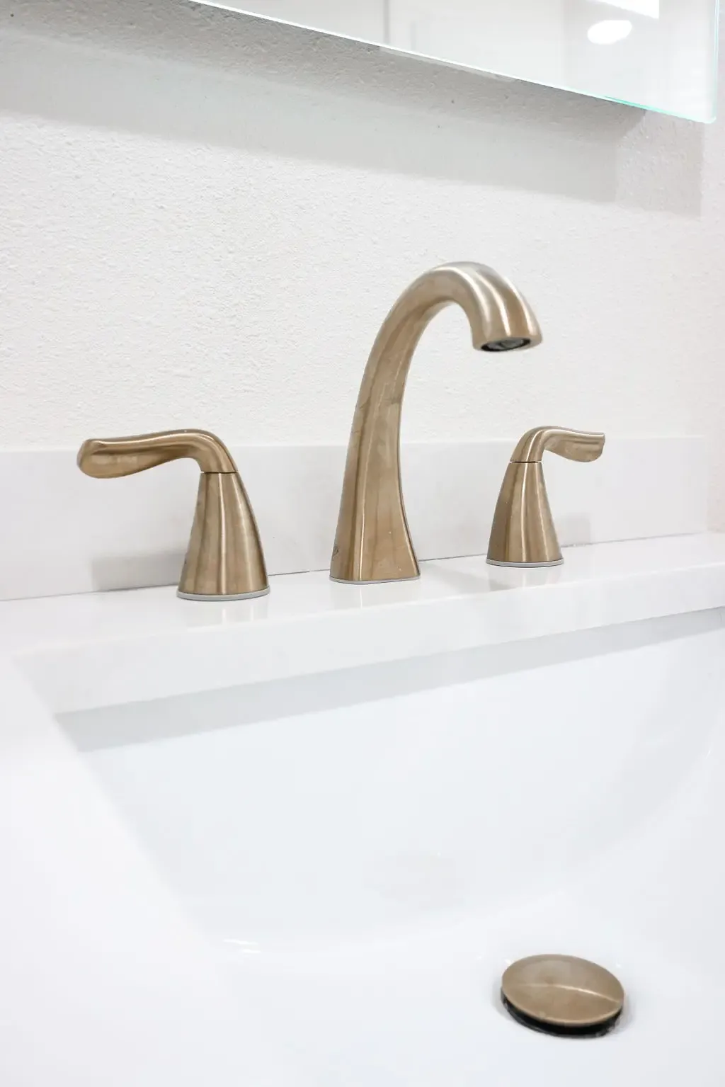Close-up of brushed bronze widespread faucet over white undermount sink and quartz counter
