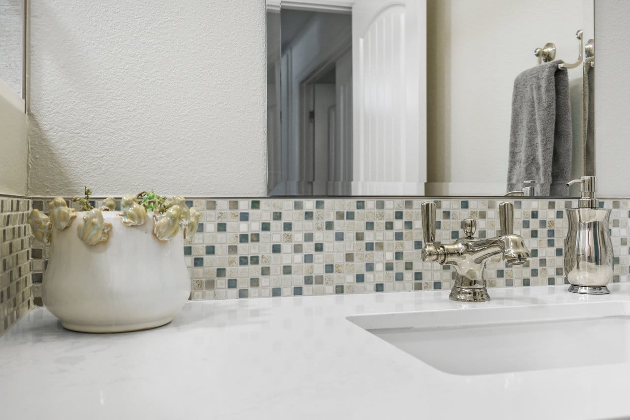 Close-up of glass mosaic tile backsplash above white quartz counter with nickel faucet