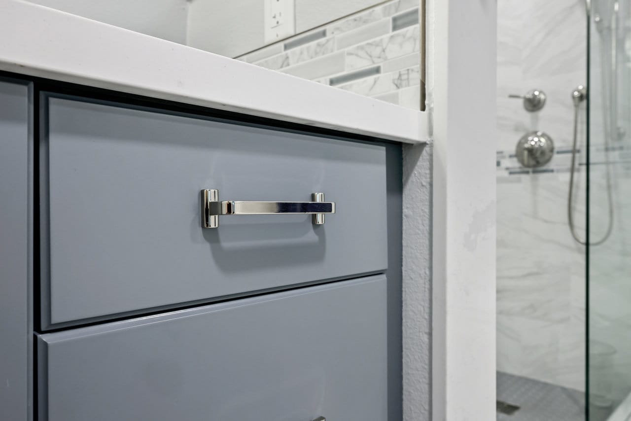close-up of gray bathroom vanity drawer with chrome pull beside glass shower