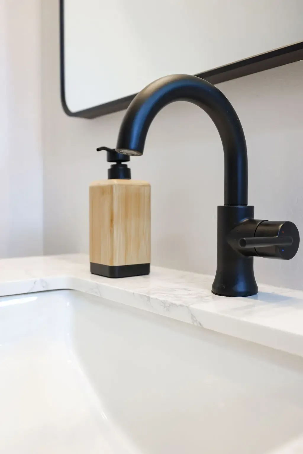 Close-up of matte black faucet on marble vanity with wood soap dispenser