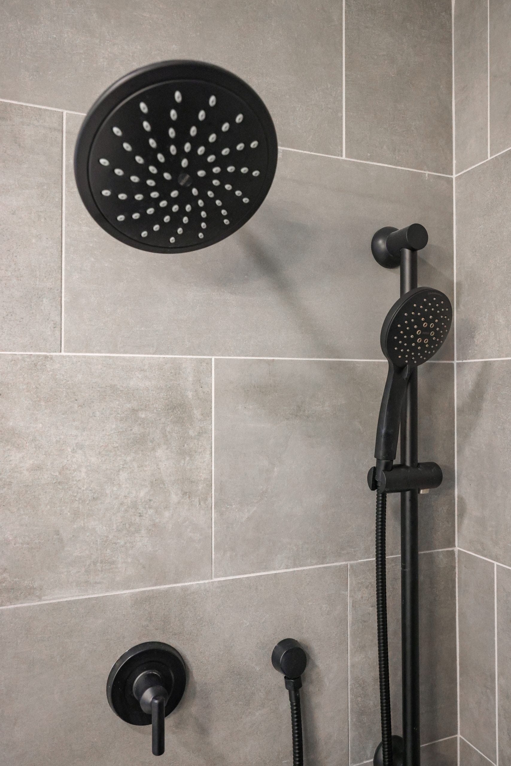 Close-up of matte black rain showerhead and handheld fixtures on gray tile