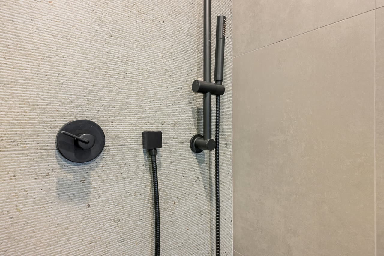 close-up of matte black shower valve and handheld slide bar on tile