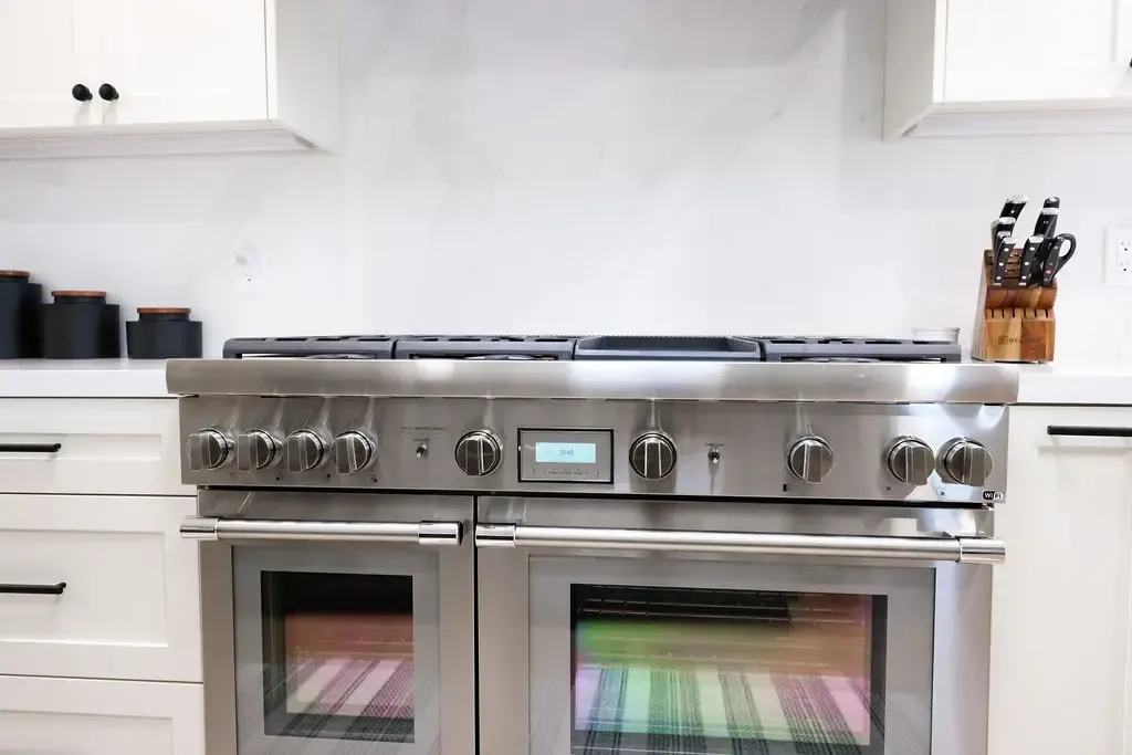 Close-up of stainless gas range and double ovens with white cabinetry