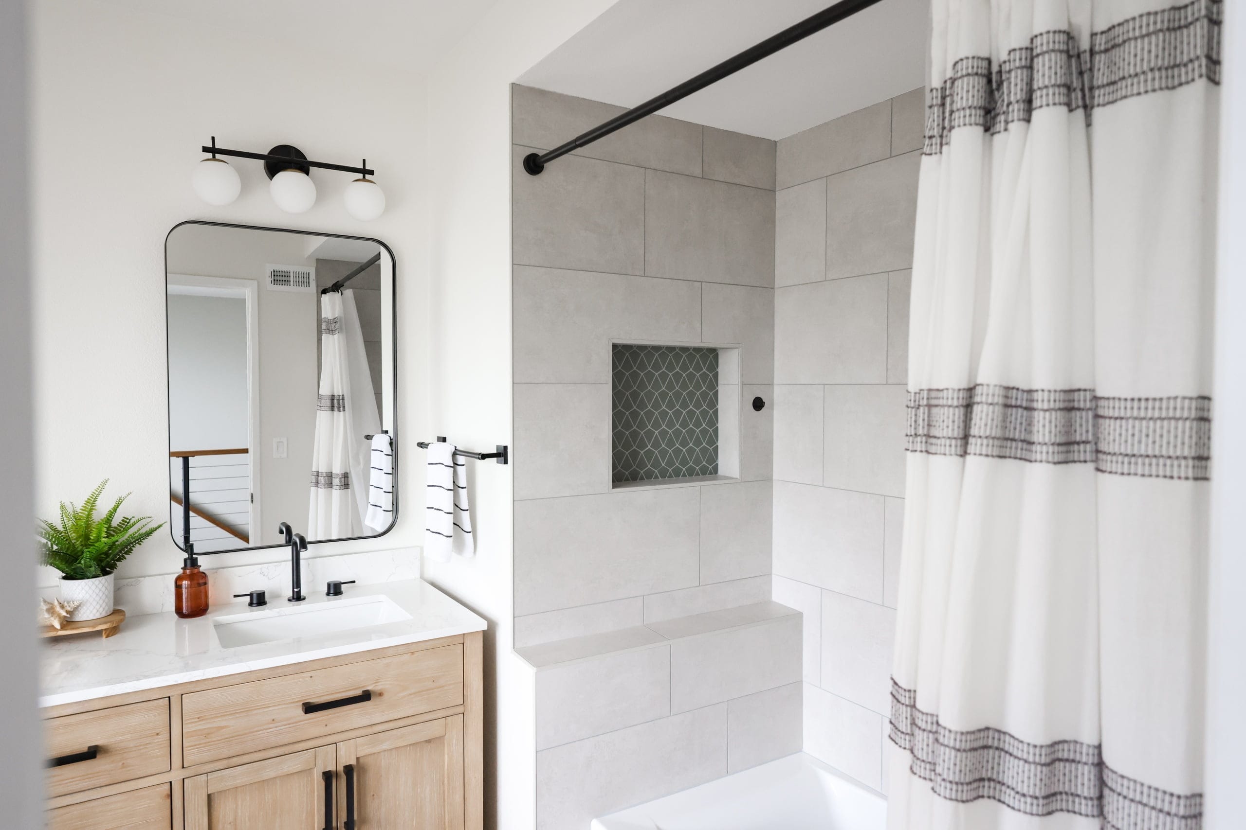 Compact bath with oak vanity, black hardware, and tiled shower-tub combo