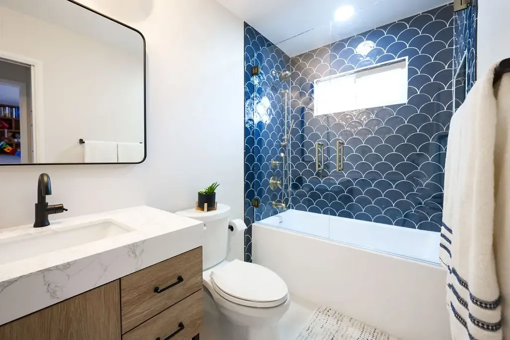 Compact bathroom with blue fish-scale tile shower surround and warm wood vanity