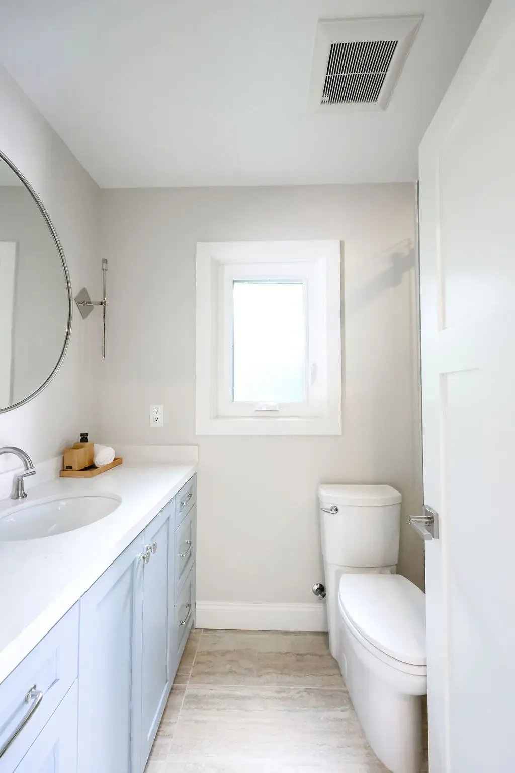 Compact bathroom with light blue vanity, round mirror and white toilet