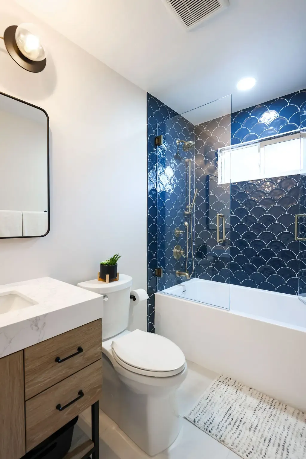 Compact bathroom with navy fishscale tile tub surround and marble-top wood vanity