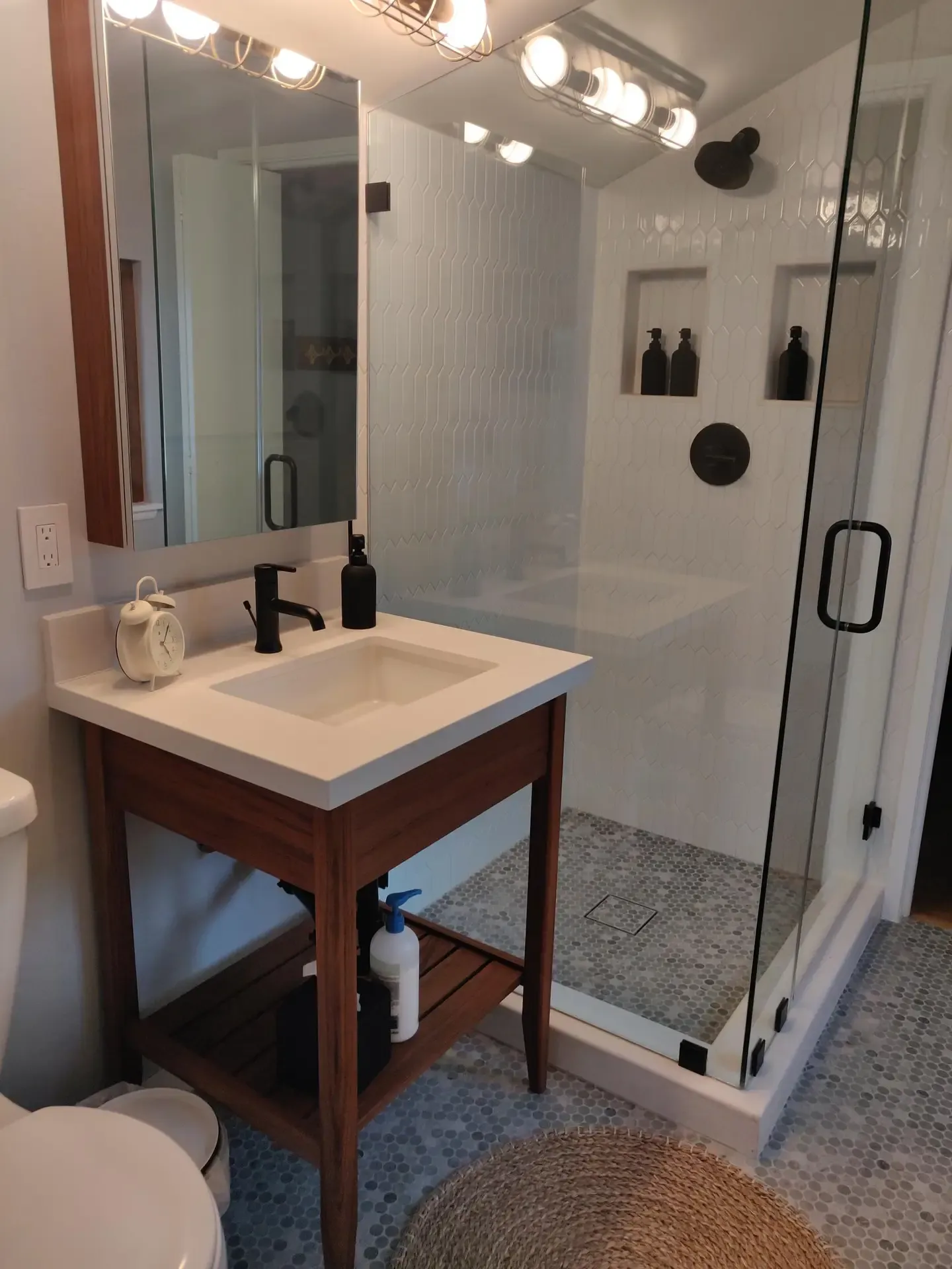 Compact bathroom with wood vanity, glass shower enclosure and white subway tile
