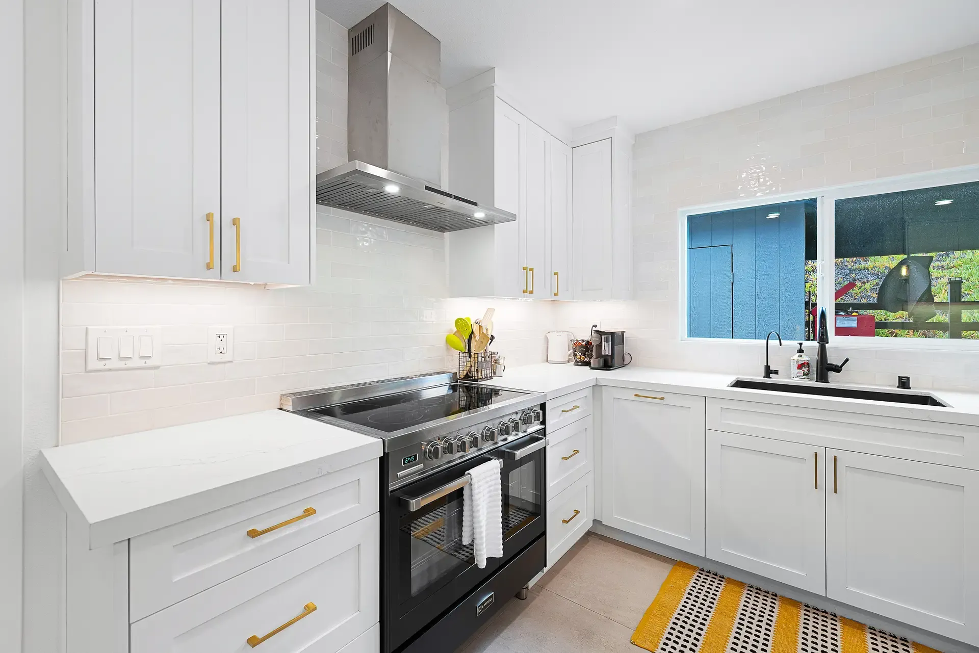 Compact white kitchen with quartz counters, black range and gold hardware