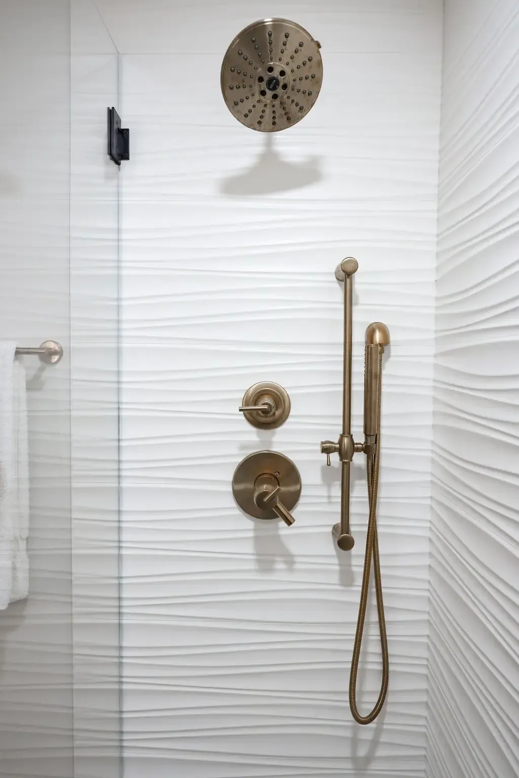 Corner shower with wavy white tile, bronze rain showerhead and handheld sprayer
