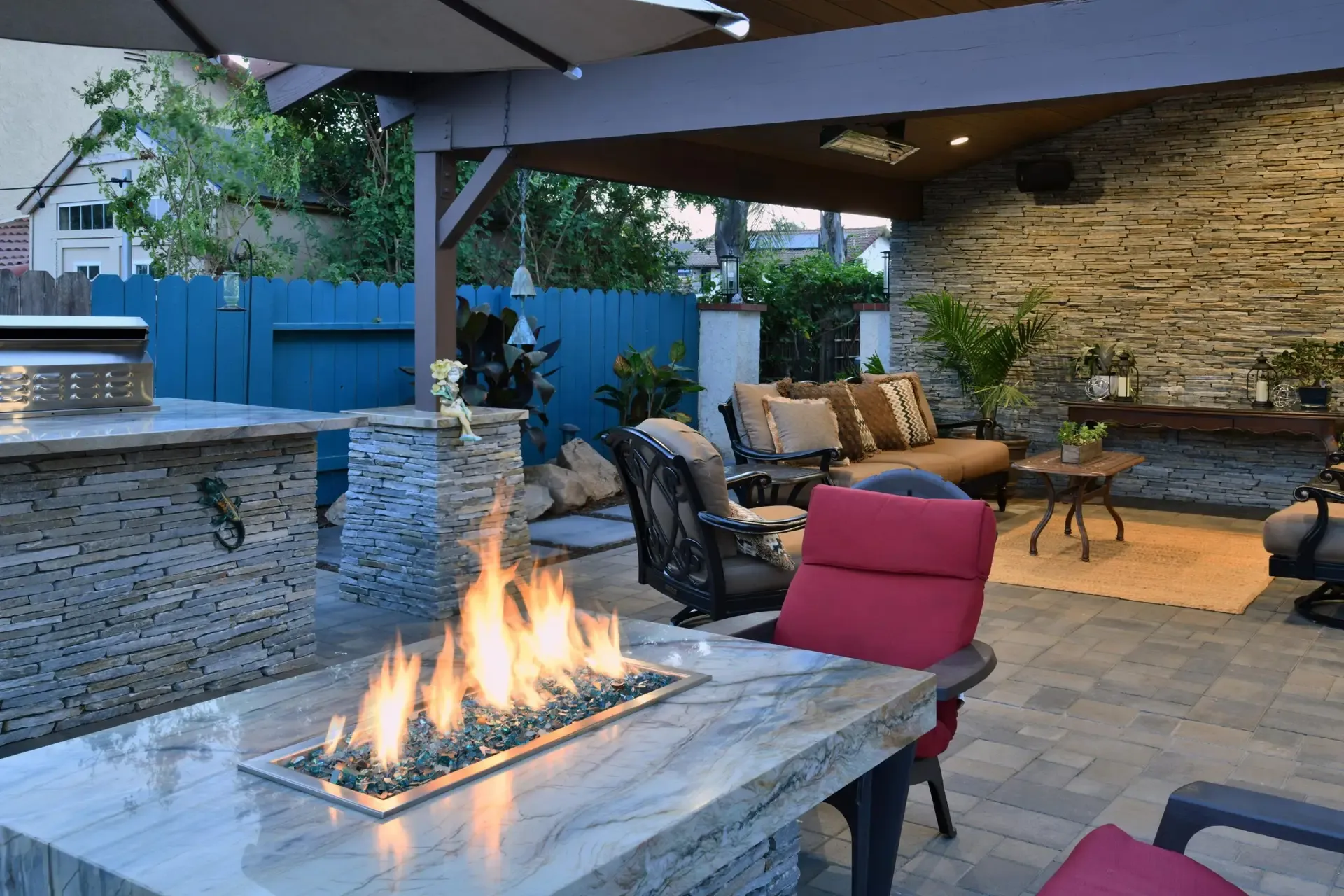 covered outdoor patio with stone fire pit table, pergola and red cushioned lounge seating