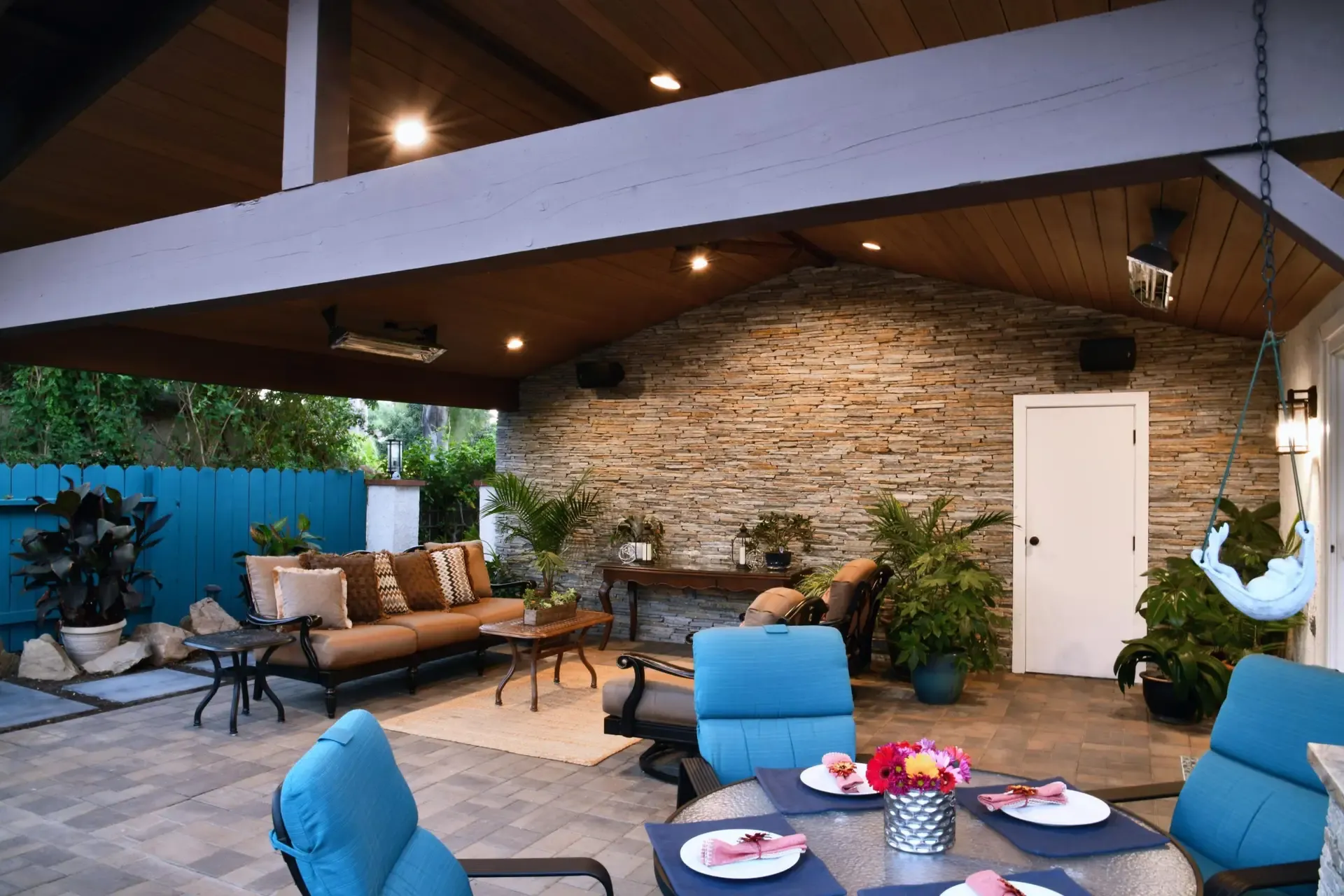 Covered outdoor patio with stone fireplace wall, wood ceiling and lounge seating