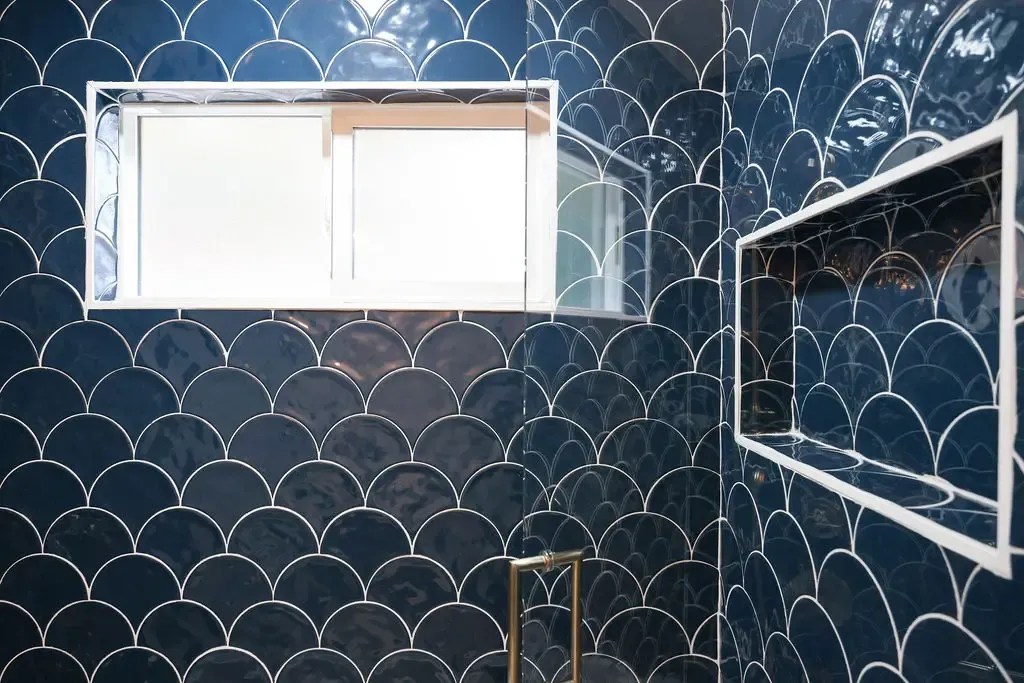 Dark navy fishscale tiled shower nook with frosted window and gold accents