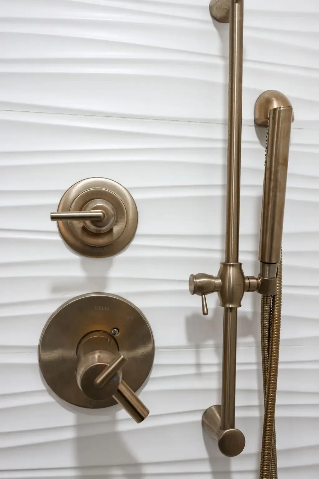 Detail of brushed bronze shower controls and slide bar on textured white tile