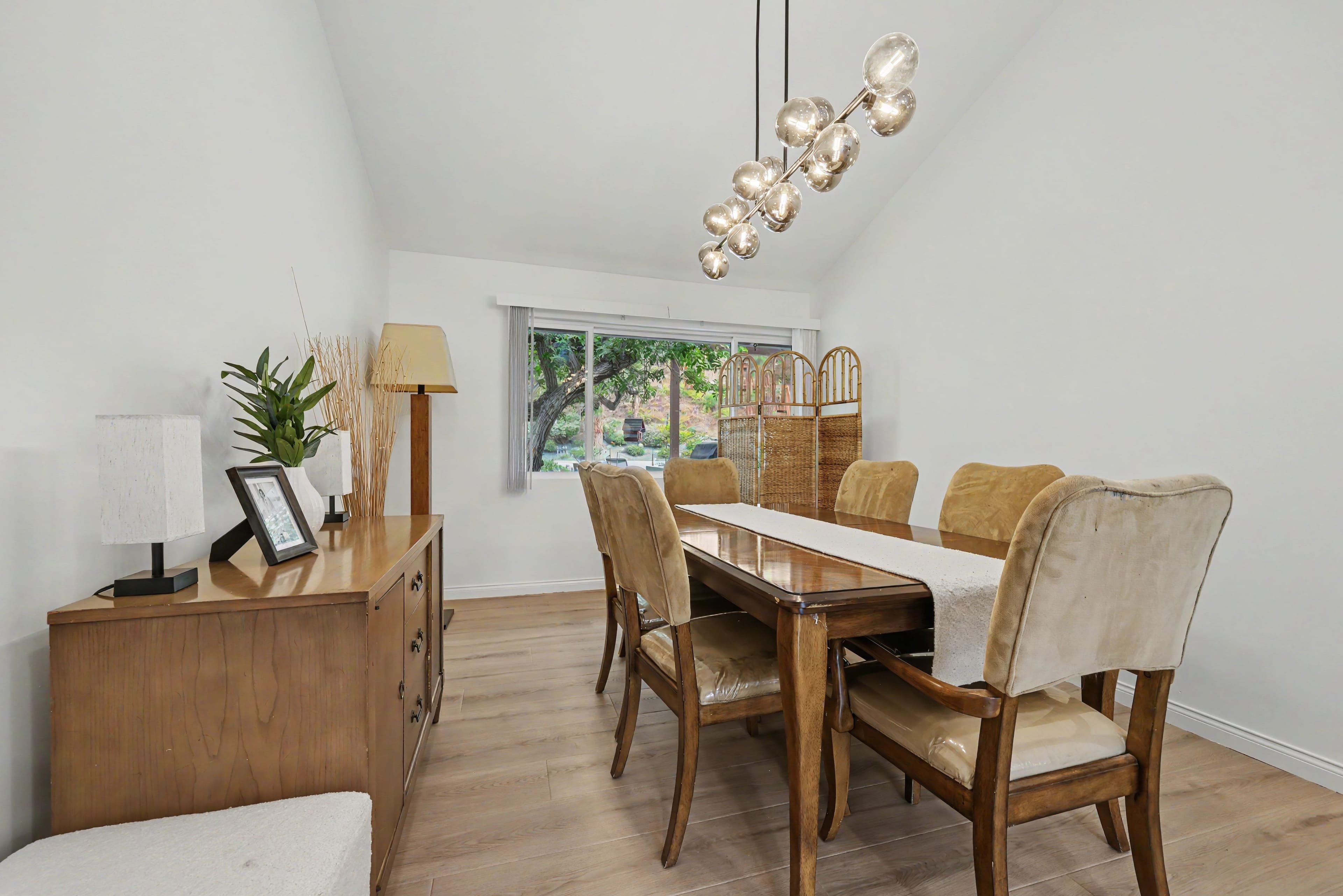 Dining room featuring a wooden table set with tan upholstered chairs, a wooden buffet cabinet, and a modern glass bubble chandelier hanging above.