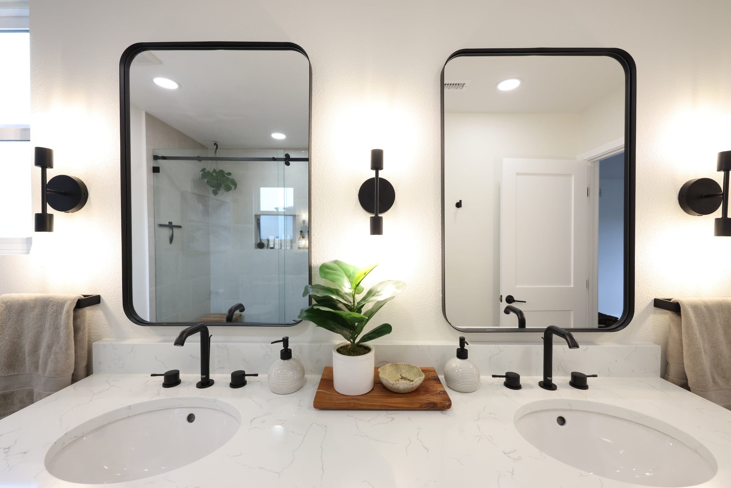Double bathroom vanity with marble counter, black framed mirrors and wall sconces