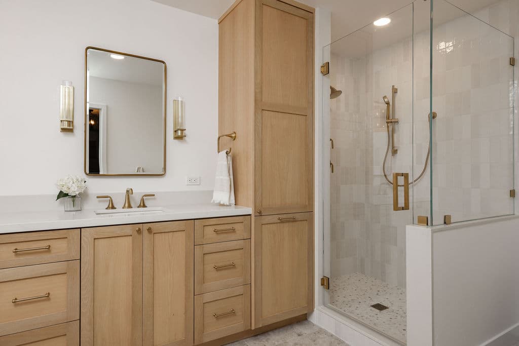 double vanity in white oak with linen cabinet and glass corner shower in stone tile