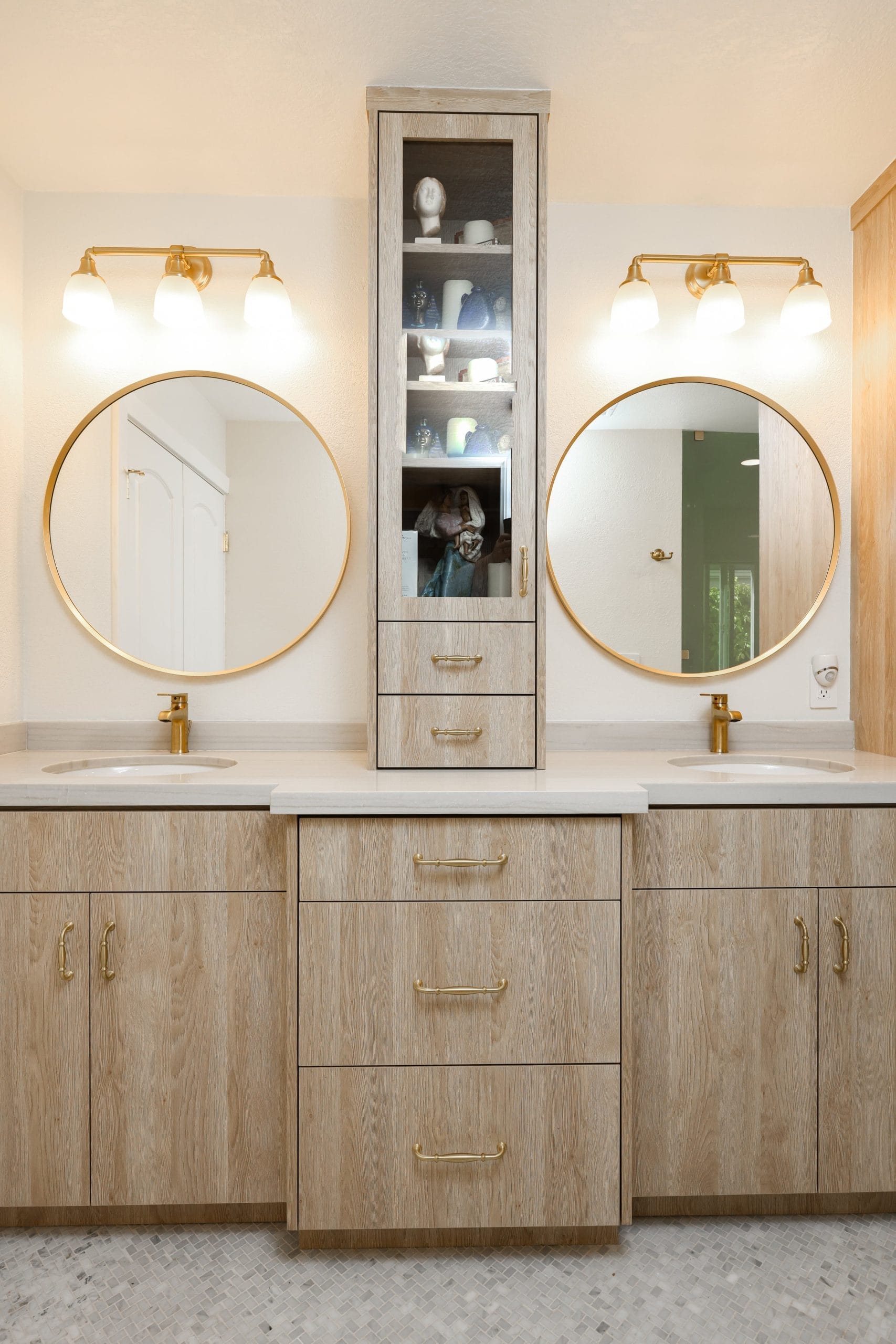Double vanity with light oak cabinets, round brass mirrors and quartz countertop