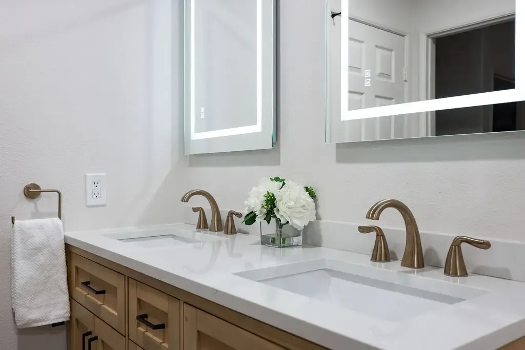 Double vanity with light oak cabinets, white quartz top and brushed brass faucets
