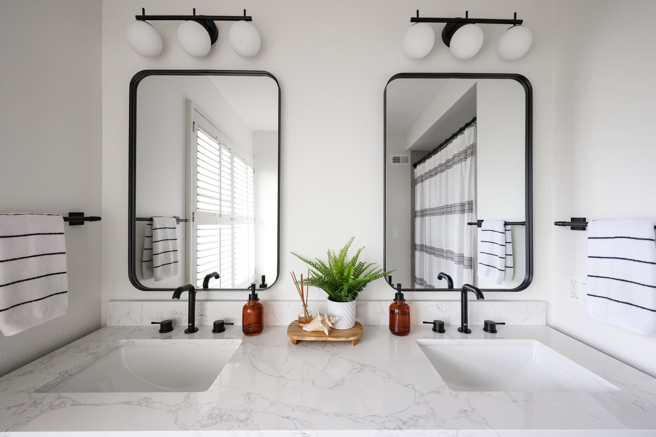 Double vanity with marble countertop, twin black mirrors, and matte-black faucets
