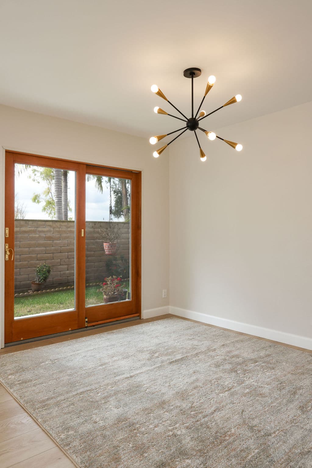 Empty room with sputnik chandelier, wood-framed patio doors and neutral area rug