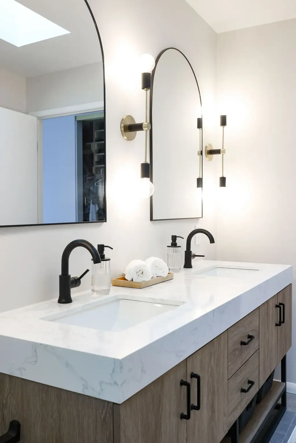 Floating wood double vanity with quartz top, black faucets and arched mirrors