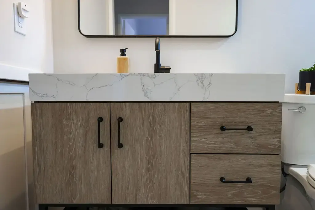 Floating wood vanity with marble countertop, black faucet and rounded mirror