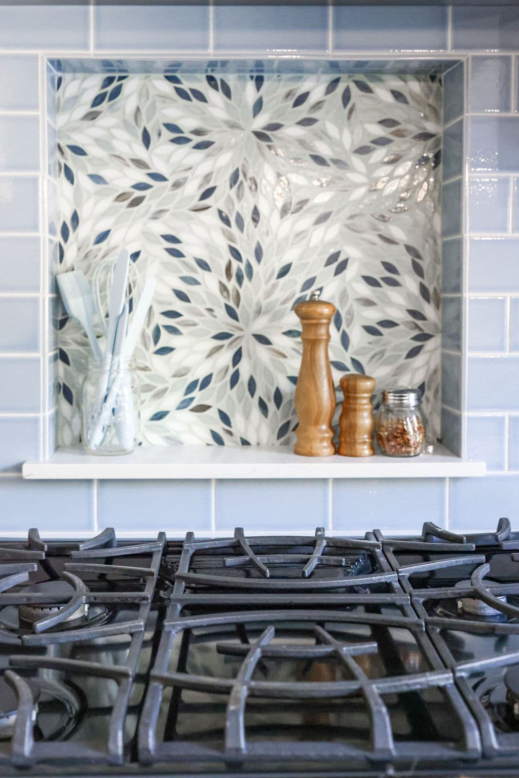 Floral mosaic backsplash niche above gas cooktop framed by pale blue subway tile