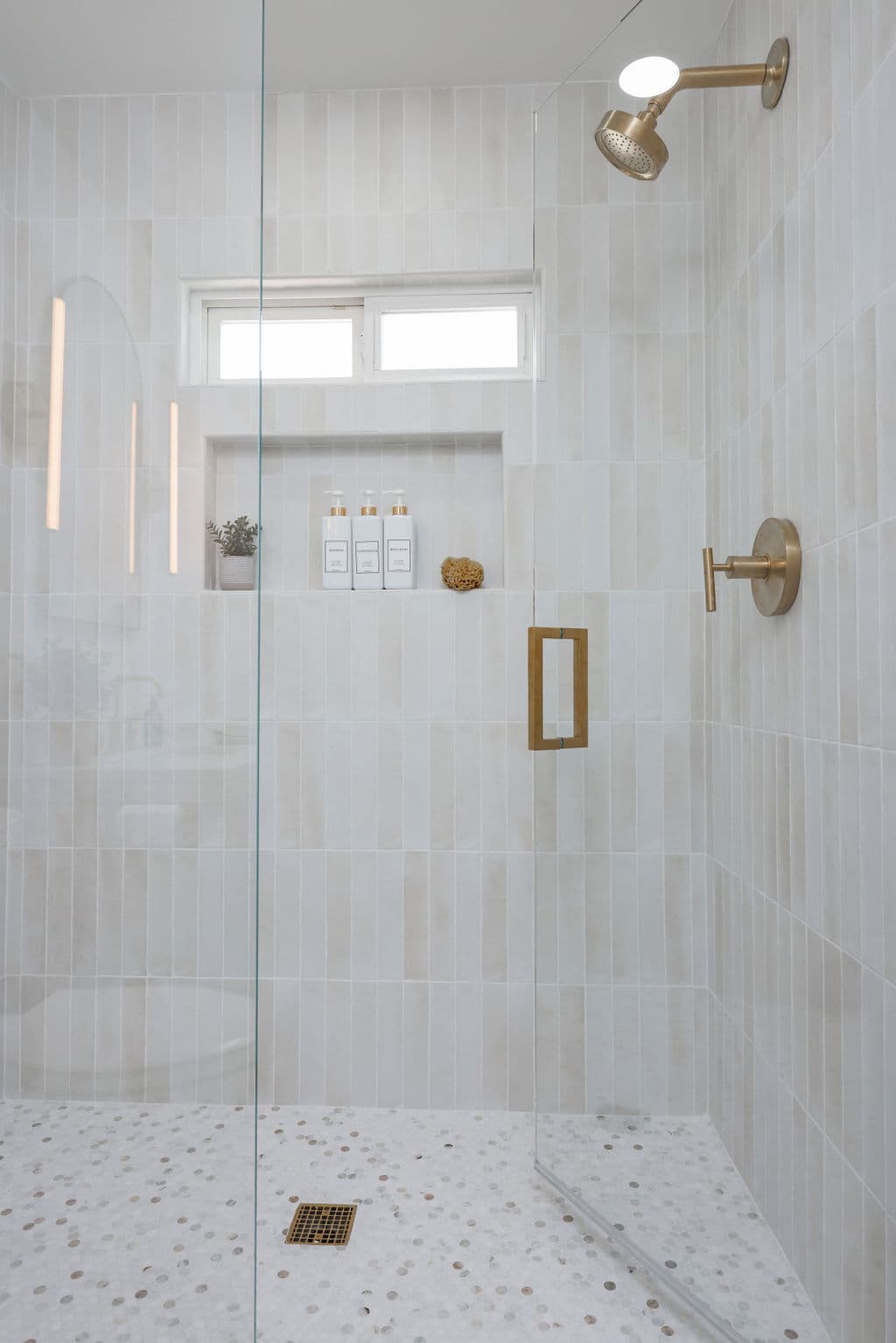 frameless glass walk-in shower with light tile, brass fixtures and pebble mosaic floor