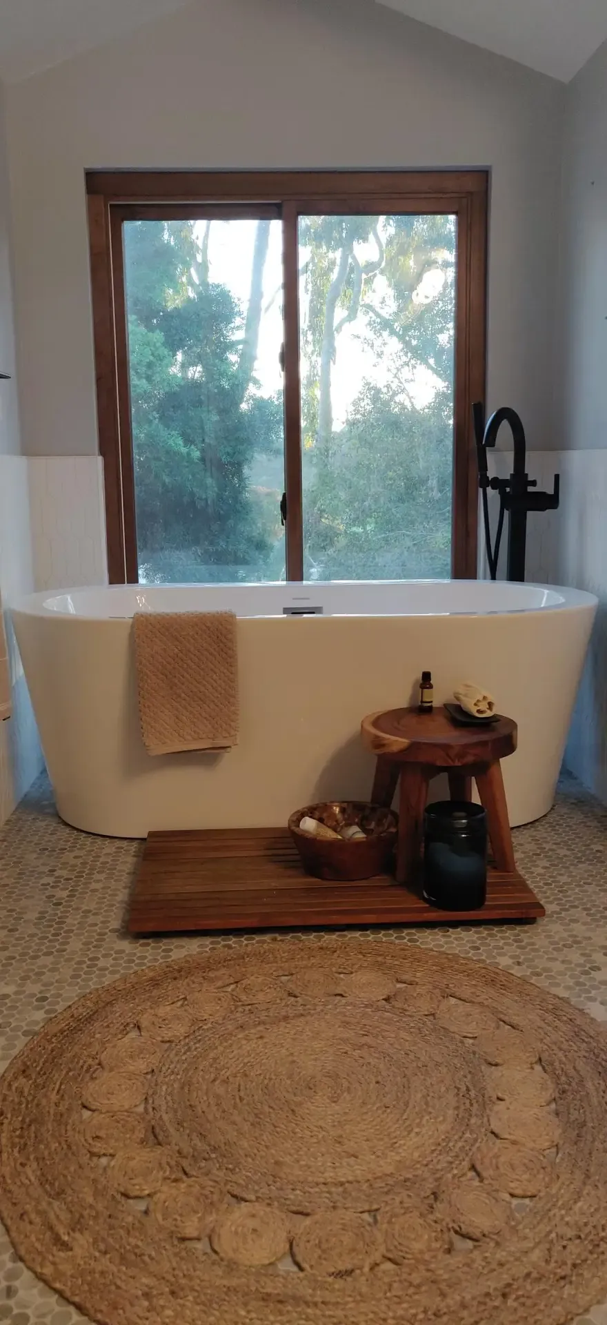 Freestanding soaking tub by window with wood trim and round jute rug