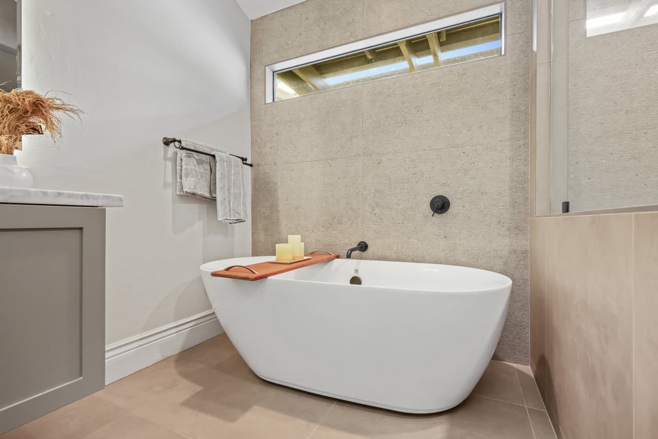 freestanding white soaking tub with black floor filler and clerestory window